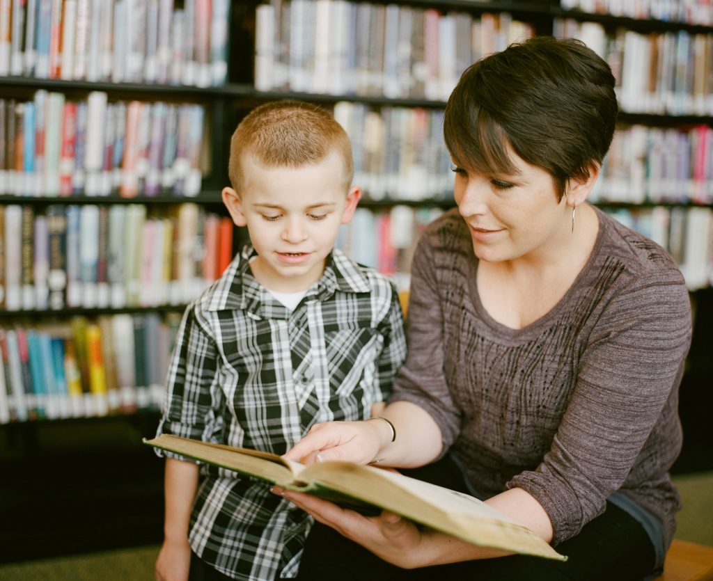 A middle-aged person is pictured showing a book to a child.