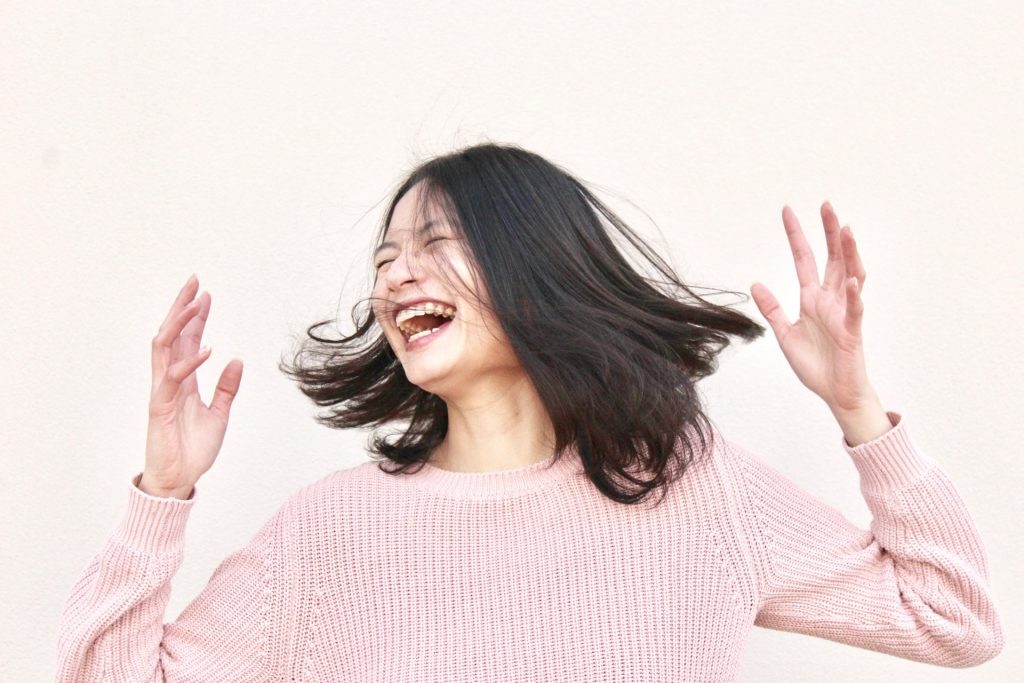 A photo of a person smiling or perhaps laughing, with their hands up, looking joyful. To truly live for yourself, you have to embrace your unique joy!