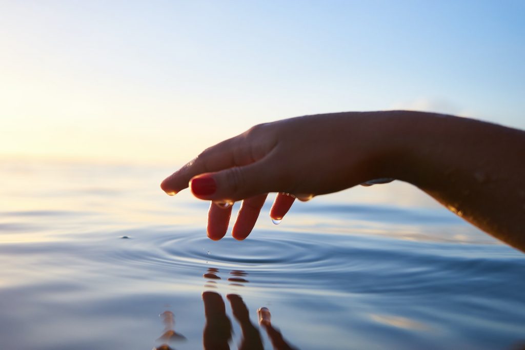 A photo of a person's hand hovering above gentle waters, a small ripple where they've just touched the water. You can use I am statements for healing.