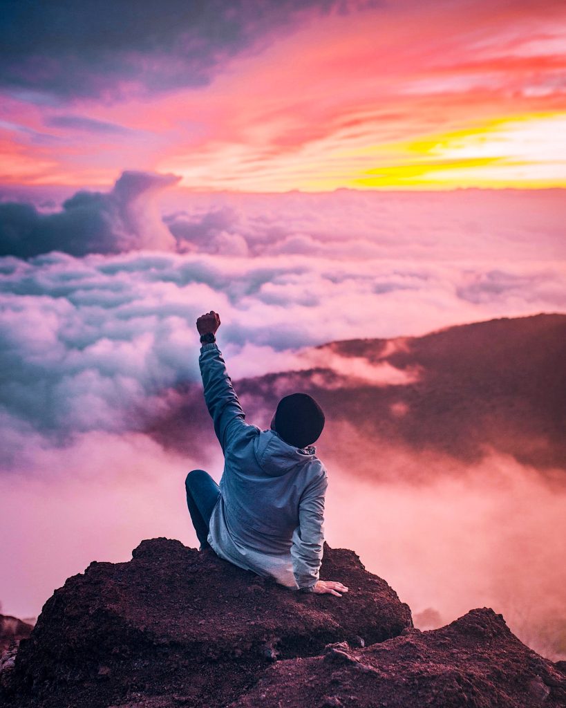 A person sits on a mountain top with their fist in the air, surrounded by a colorful sunset amongst the clouds. When starting something new, it's important to remember your inspiration.