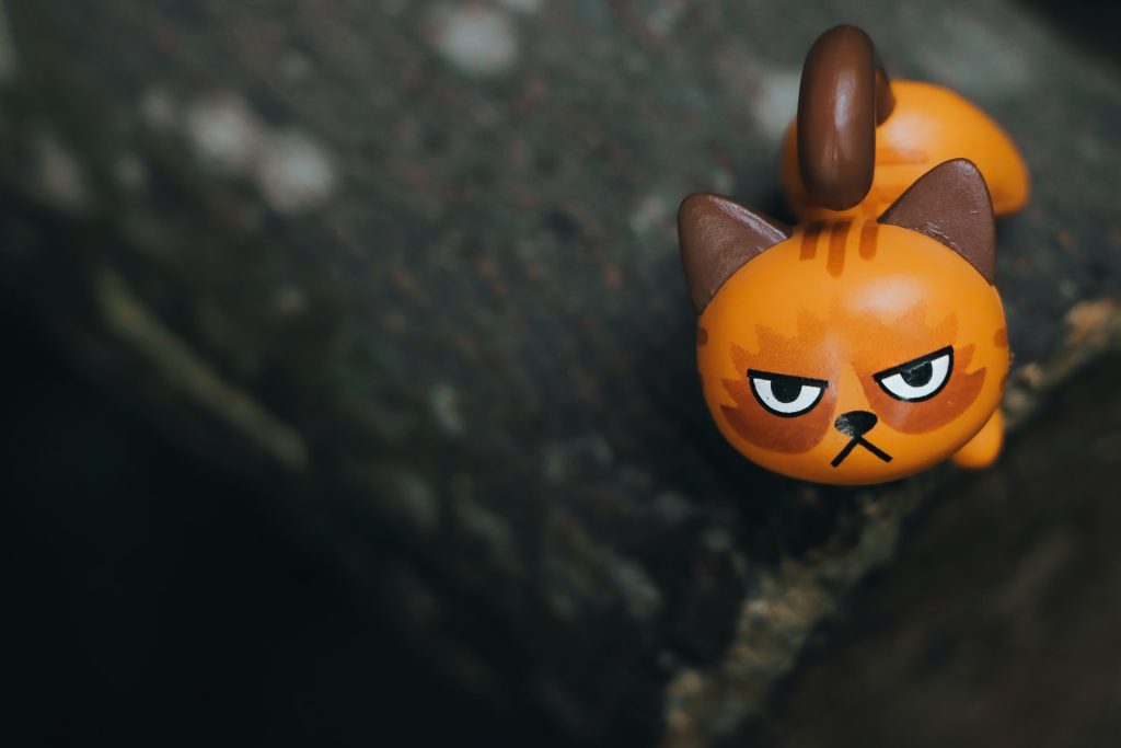 A close-up photo of a figurine of an angry looking orange cat. Anger affirmations can help in coping with anger.