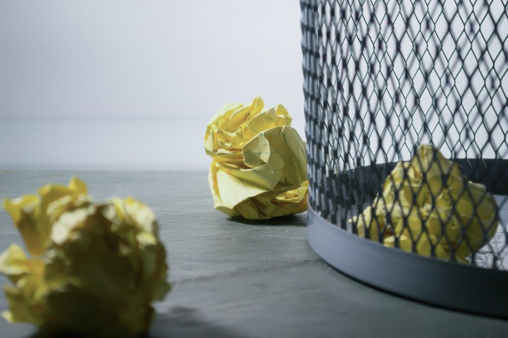 Three crumpled pieces of yellow note paper are in and around a waste basket. When it comes to perfectionism, affirmations can help!