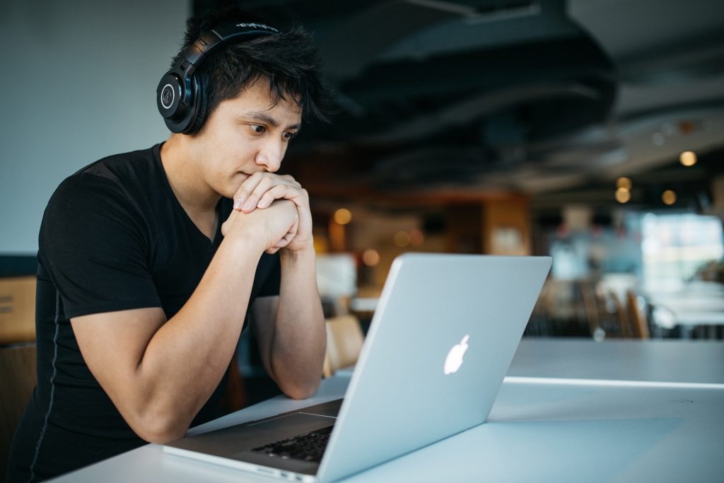 A photo of a person sitting at their laptop with headphones on, looking interested and focused on learning.