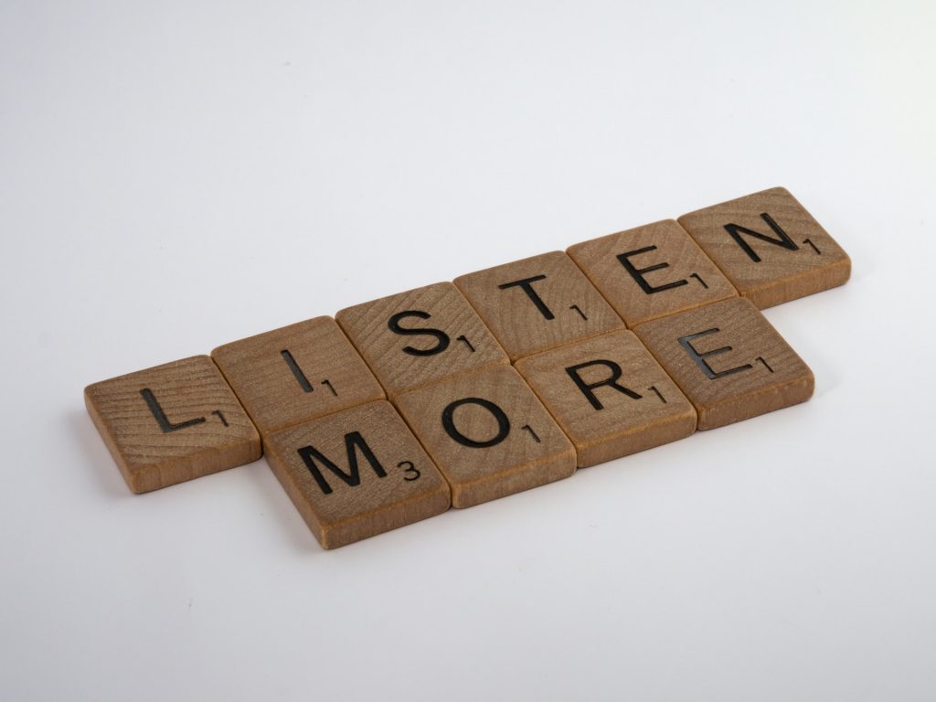 A photo of scrabble pieces on a white background, spelling out the words "listen more".