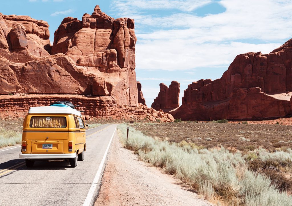 A photo of a yellow van on a road trip amongst red rocks.