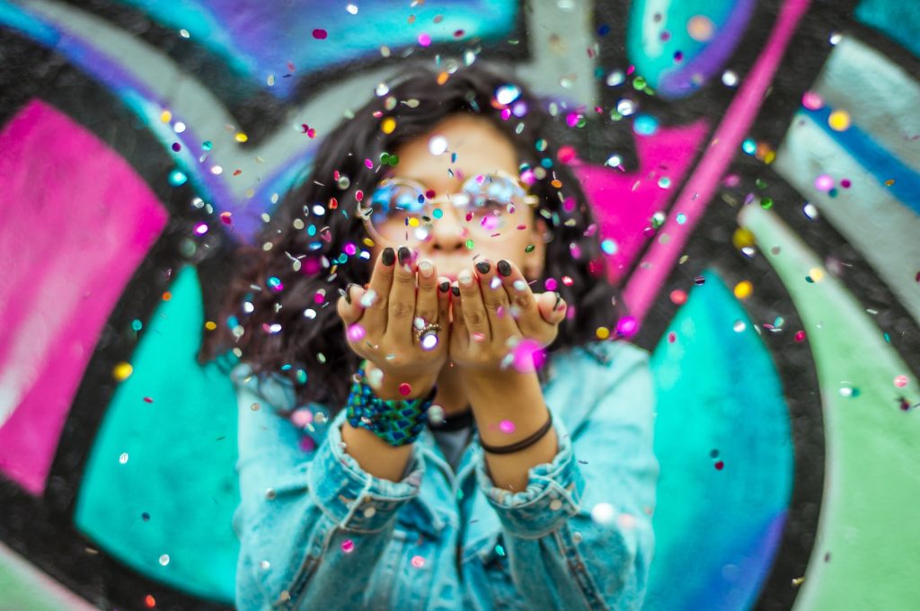 A bright and colorful photo of a person blowing confetti into the camera.