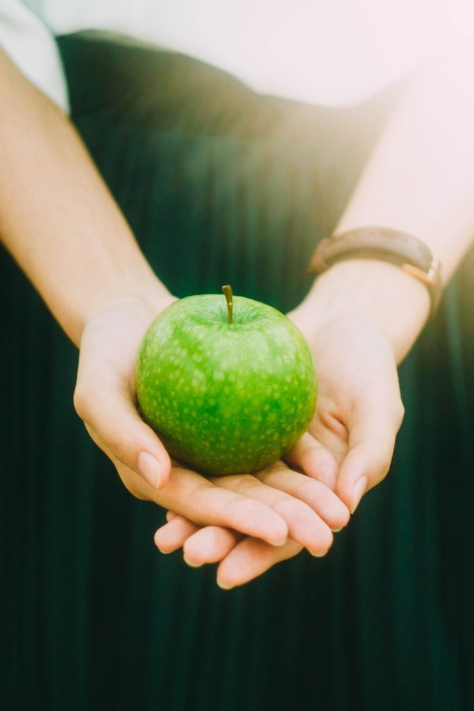 A photo of a person holding out a green apple, cupped in both hands.