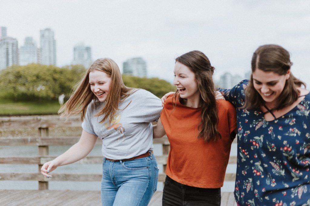 A photo of a trio of friends walking outside arm in arm and laughing.
