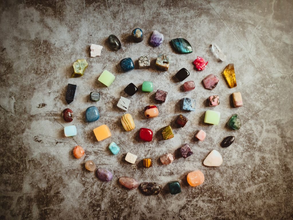A variety of gemstones and crystals arranged in a spiral on a concrete gray background. Once you have affirmations for crystals you can carry them around to help with grounding and inspiration throughout the day.