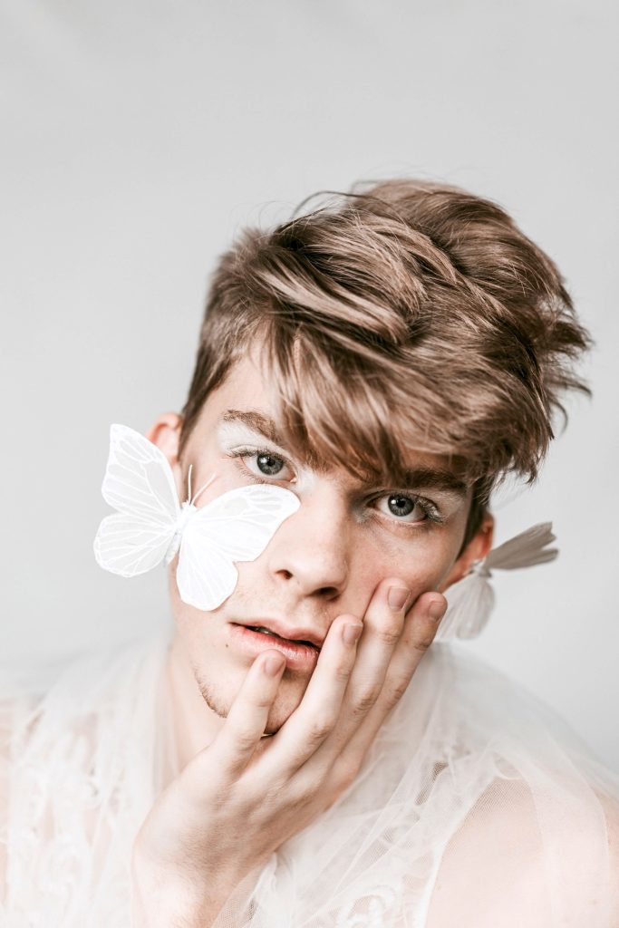 A close up photo of a person with short hair, with fake white butterflies on their face. Beauty within is important when focusing on affirmations for beauty.