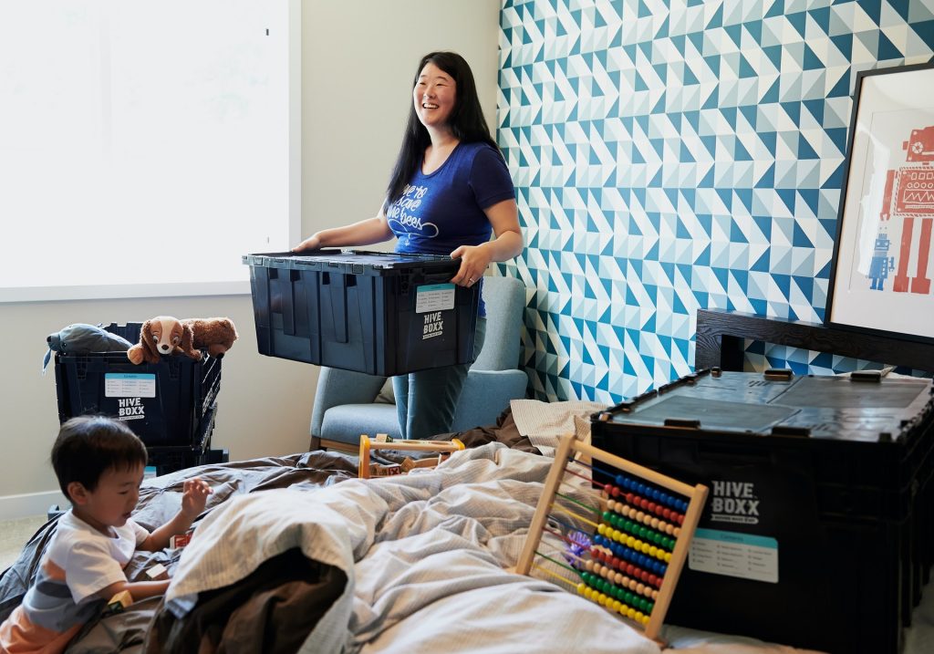 A photo of a person holding a box of things, with other boxes scattered about the room. Sorting through your things is one of the first steps for how to organize your life in one week.