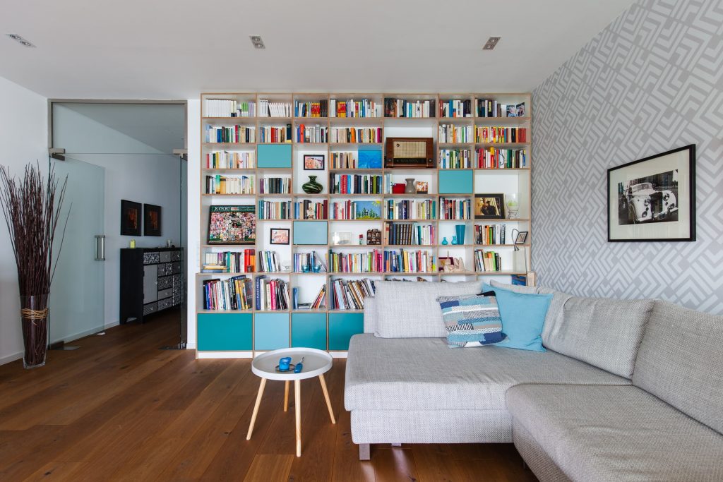 A photo of a living room with a wall of shelves, filled with books. When learning how to organize your life in one week, setting aside time for organizing your physical space is the first step.