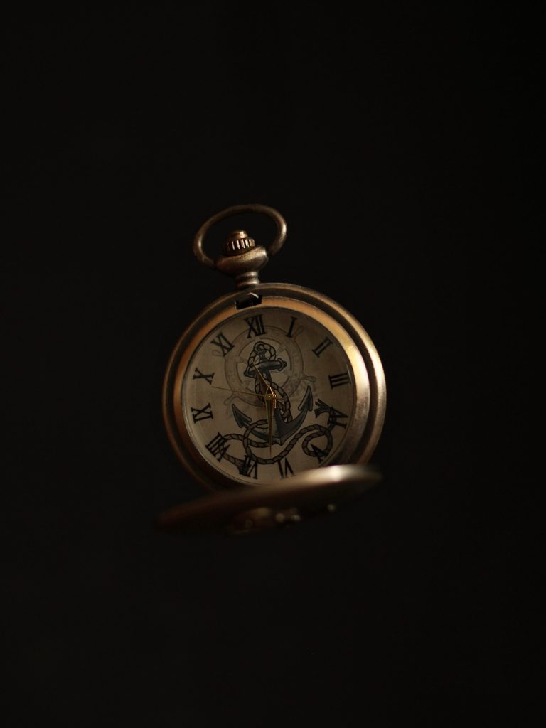 A photo of an open pocket watch amidst a black background. There's an illustration of an anchor, a rope, and a ship's steering wheel on the face of the clock. The golden clock hands indicate that the time is just past eleven thirty. A mindful evening routine works best when set at the same time every night.