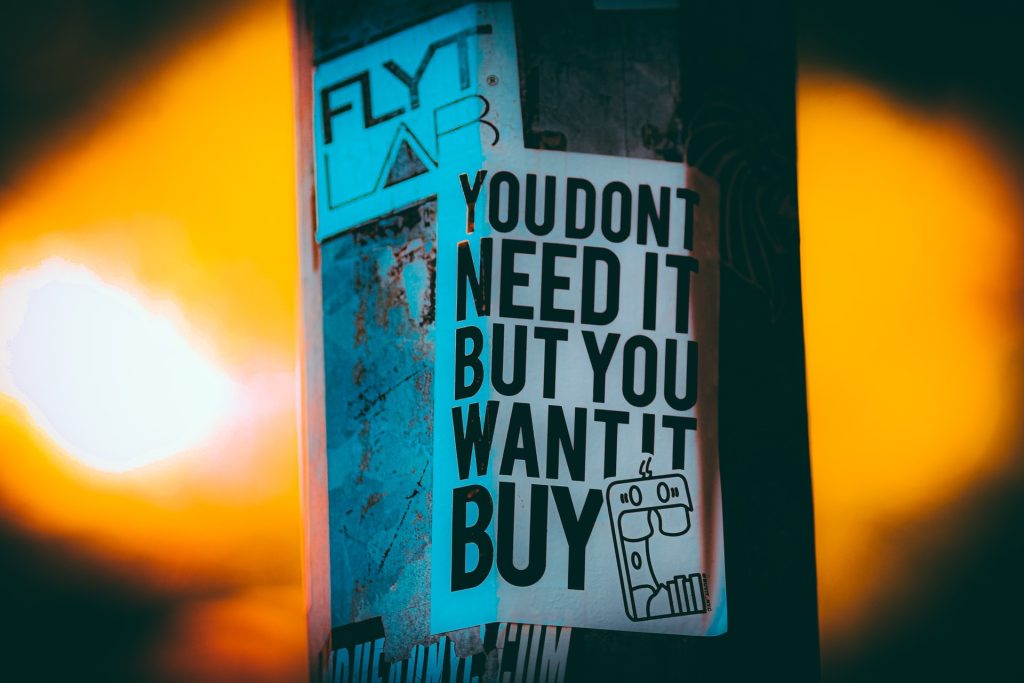 A photo of a paper sign taped to a pole. The sign reads: You don't need it but you want it. Buy.
