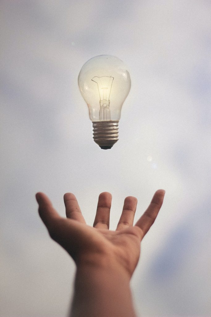 A photo of an outstretched hand with a lightbulb hovering above it. Positive affirmations for creativity can also include creative thinking!