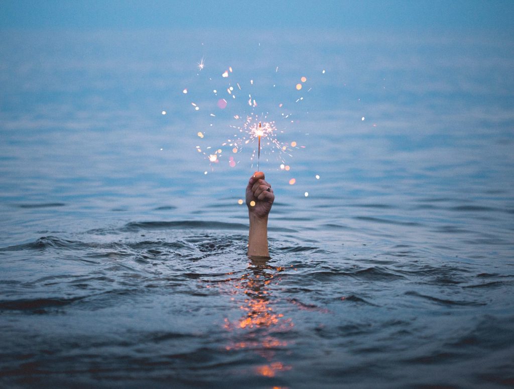 A photo of a hand sticking up out of the water, holding a sparkler. We can't have creativity affirmations without some I am Creative affirmations to remind you of that creative spark inside you!