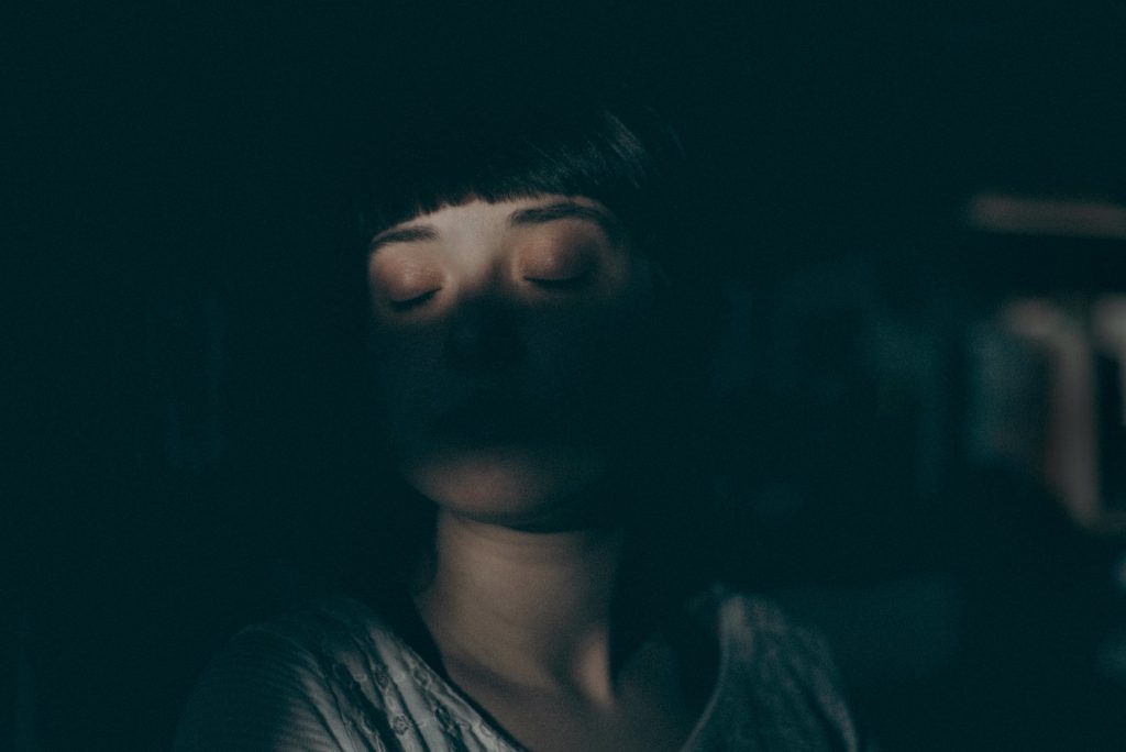 An artistic photo of a person closing their eyes, with shadows obstructing the rest of their face.